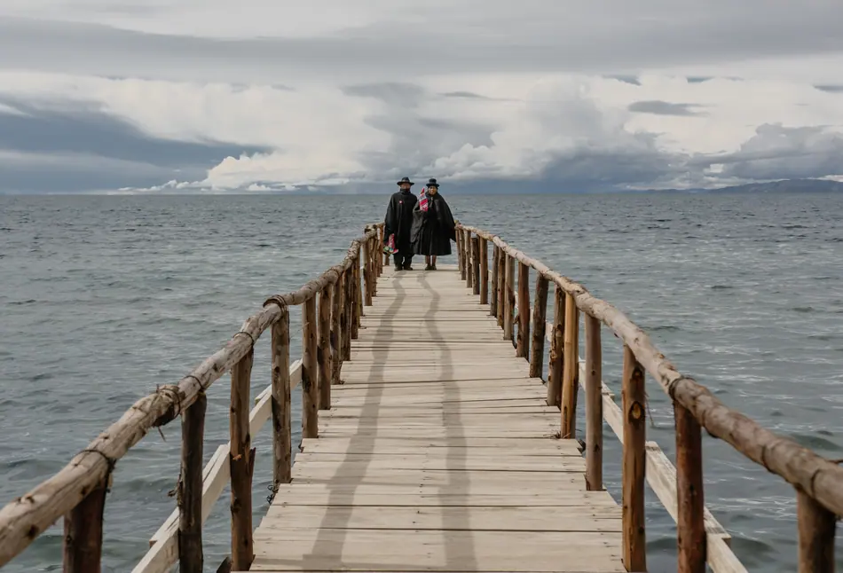 Muelle de madera adentrándose en el lago Titicaca con figuras al fondo